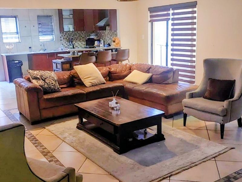 Open-plan living area featuring tiled floors, a brick fireplace, and a connected kitchen with built-in cabinetry and an island, leading to a patio area.