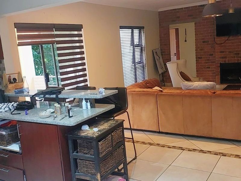 Open-plan living area featuring a kitchen with stone countertops and a breakfast bar, flowing into a lounge with a brick fireplace.