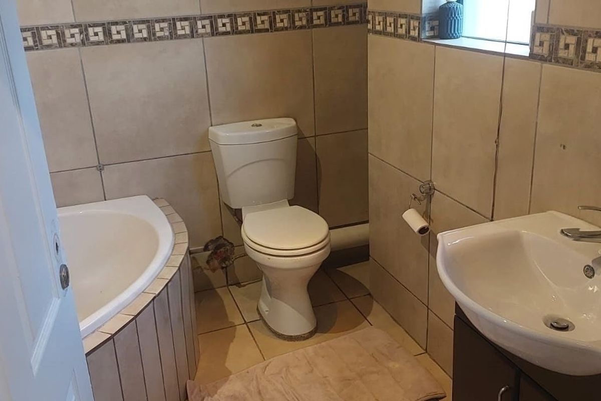 A functional bathroom featuring a corner bathtub, toilet, and vanity basin with tiled finishes throughout.