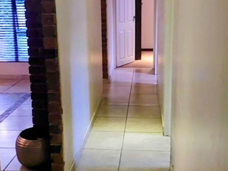 A bright, tiled hallway featuring an exposed brick accent pillar and recessed lighting, providing a clean transition between living spaces.