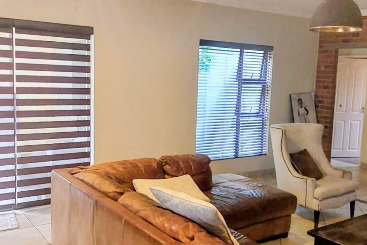Spacious living room featuring a brick fireplace, tiled flooring, and large sliding doors with modern blinds, offering a comfortable and well-lit living space.