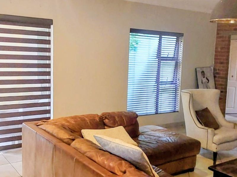 Spacious living room featuring a brick fireplace, tiled flooring, and large sliding doors with modern blinds, offering a comfortable and well-lit living space.