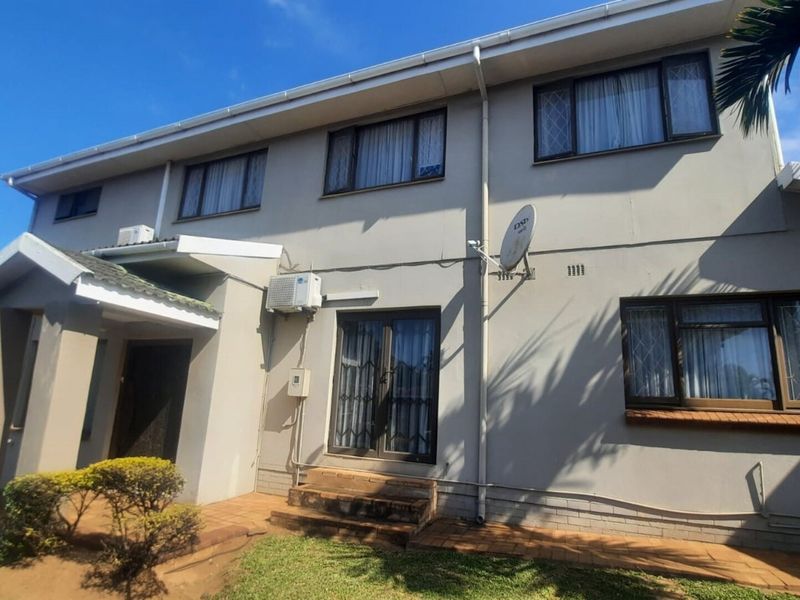 Rear exterior view of the townhouse featuring a paved walkway, sliding glass door with security gate, and wall-mounted air conditioning unit.