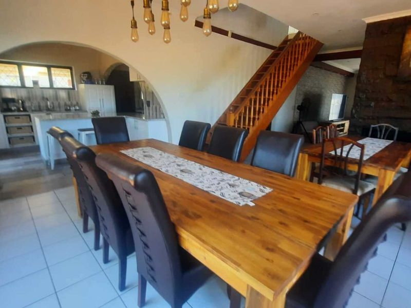 Open plan dining area featuring a wooden staircase, stone feature wall, and arched transition to the kitchen space with tiled flooring throughout.
