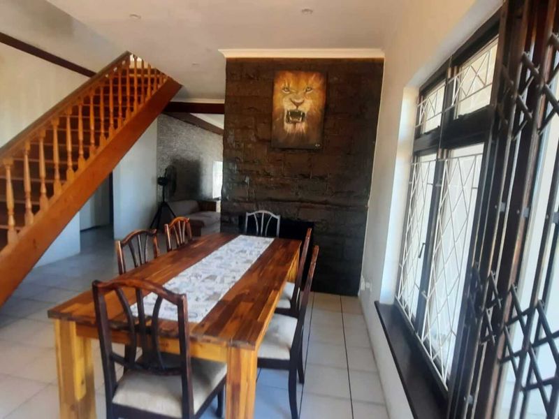 Dining area featuring a prominent stone accent wall, tiled flooring, and a wooden staircase leading to the upper level.