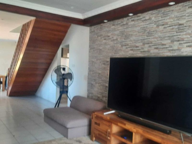 Spacious living area featuring a textured stone accent wall, wooden staircase, and tiled flooring, offering a warm and inviting atmosphere.