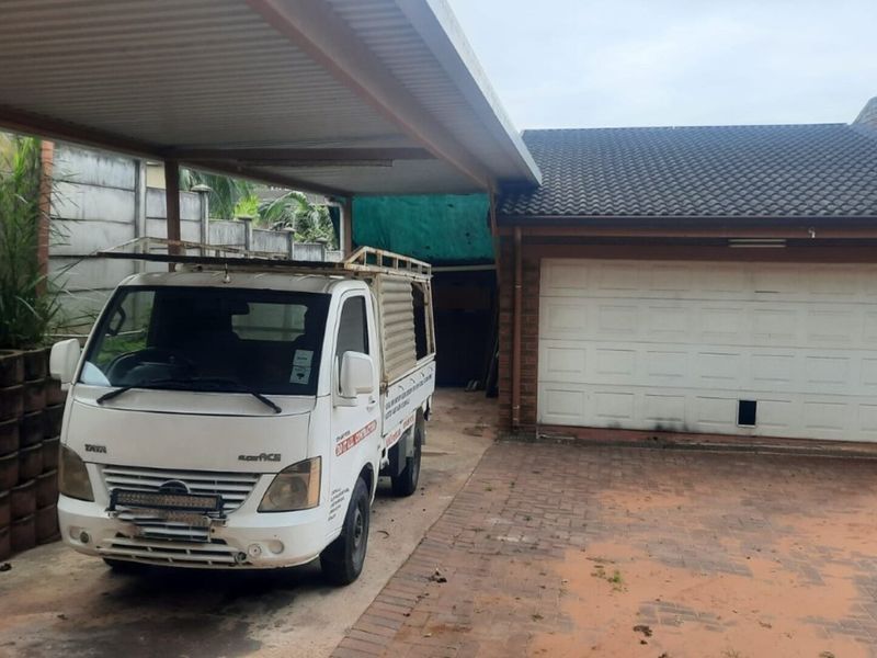 Exterior view of a residential property featuring a covered carport area and a sectional garage door with brick paved driveway.