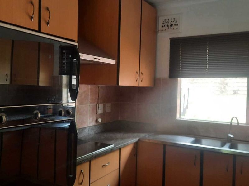 A functional kitchen featuring built-in oven, extractor fan, double sink, and laminate cabinetry with tiled backsplash, offering potential for modern updates.