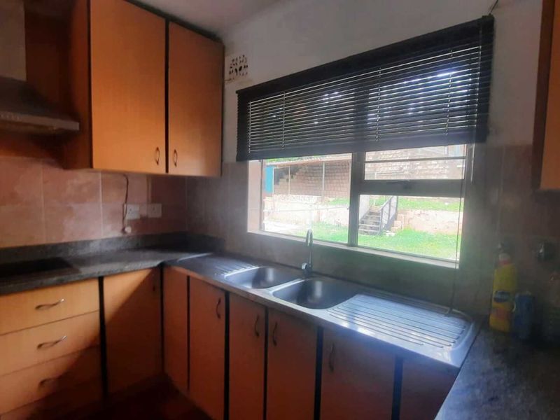 A functional kitchen featuring wooden cabinetry, stone countertops, a double stainless steel sink, and an integrated extractor fan with a view to the exterior.