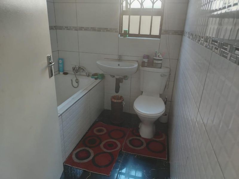 A compact bathroom featuring a bathtub, pedestal basin, and toilet with tiled walls and flooring.