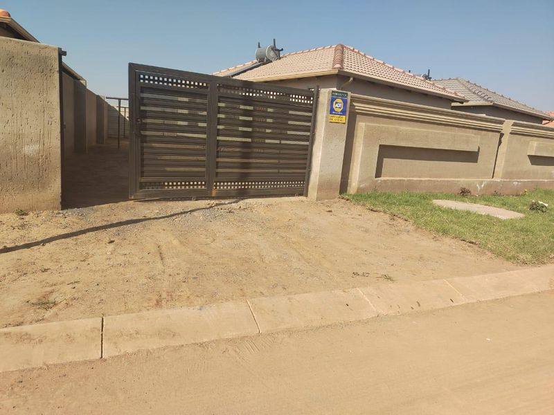Front exterior view of the property featuring a secure sliding gate, perimeter wall, and solar geyser installation on a tiled roof.