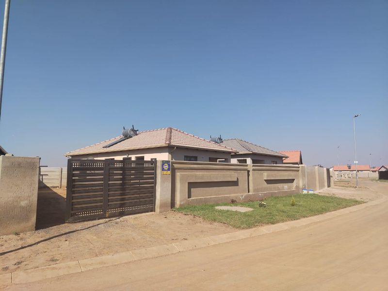 Front view of a residential property featuring a perimeter wall, metal gate, and solar water heating system on a tiled roof.