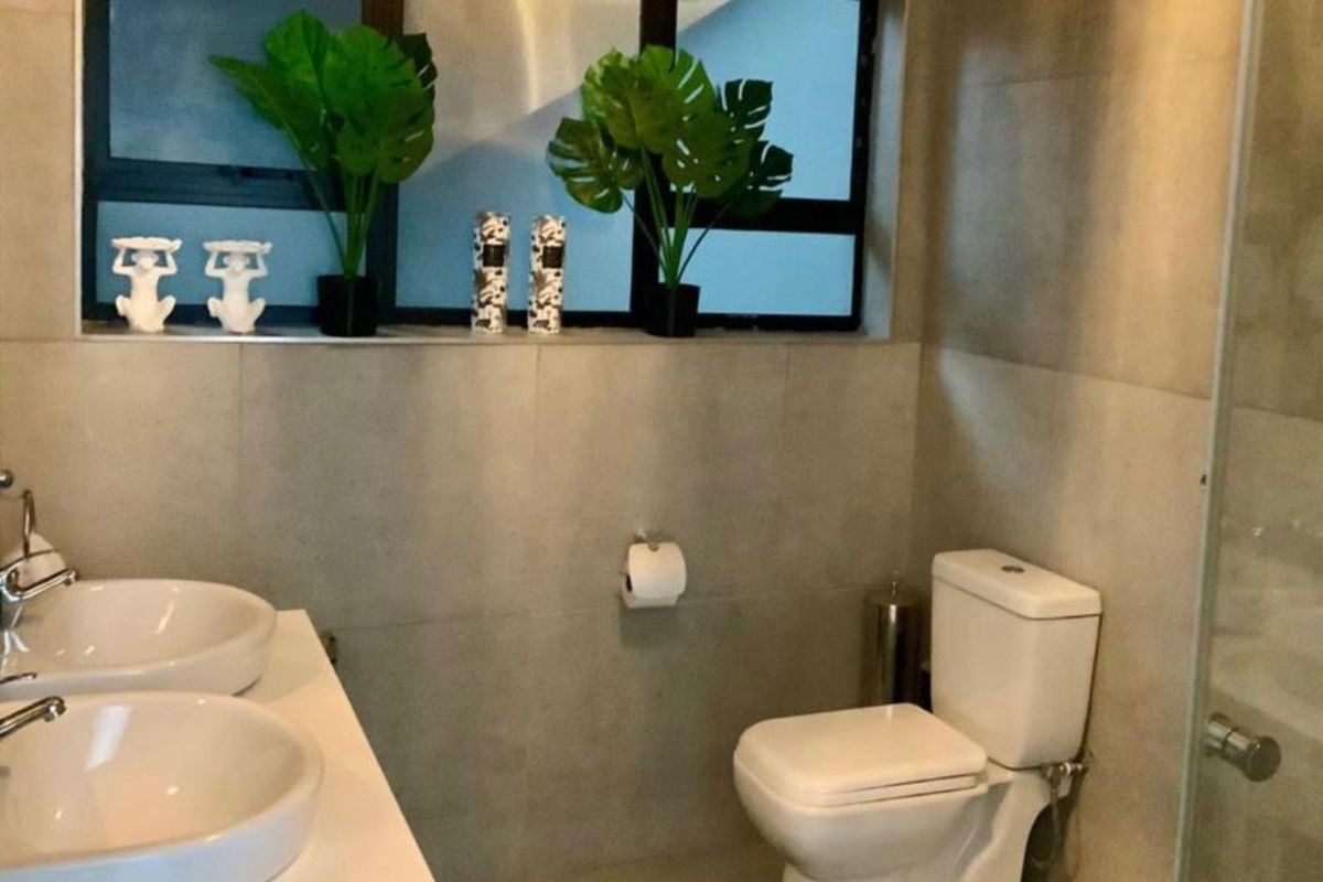 Modern bathroom featuring a double vanity with ceramic basins, tiled walls, and a shower enclosure with an aluminium-framed window.