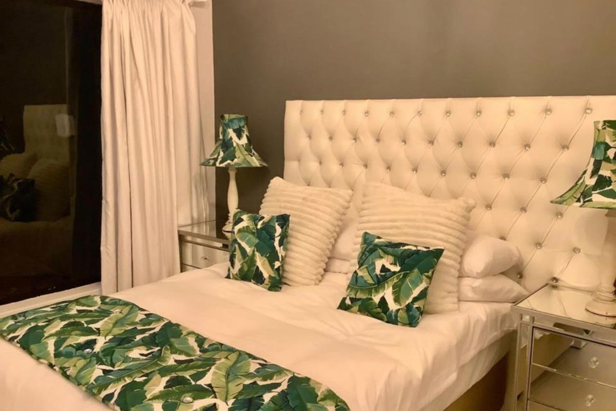 A cozy bedroom featuring a large, tufted white headboard and neutral wall tones, creating a comfortable and inviting sleeping space.
