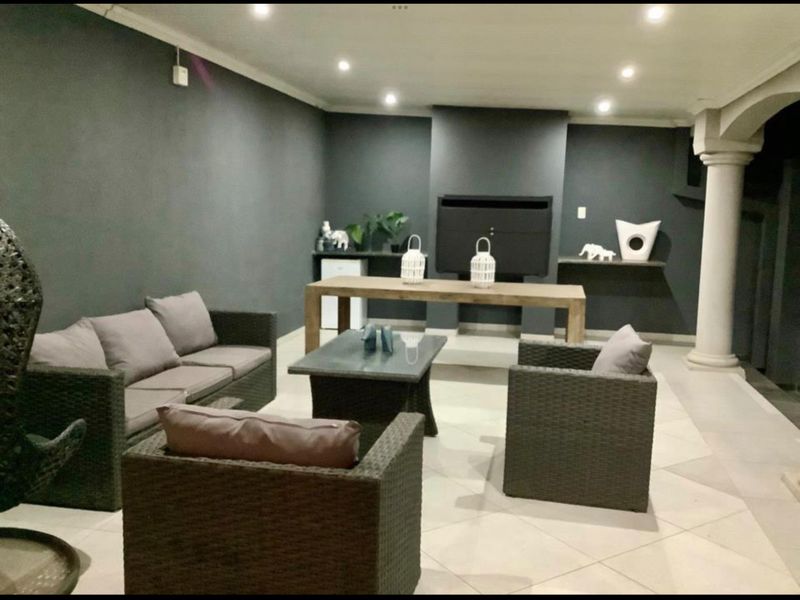 A covered patio area featuring a built-in fireplace, recessed lighting, and tiled flooring, providing a functional space for outdoor entertainment.