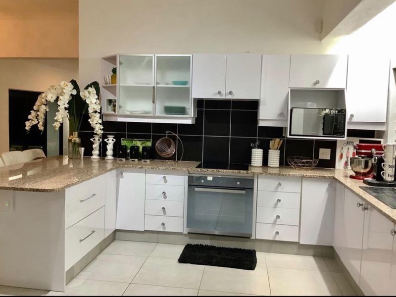 A modern kitchen featuring white cabinetry, granite countertops, a built-in oven, and a contrasting black tiled backsplash.