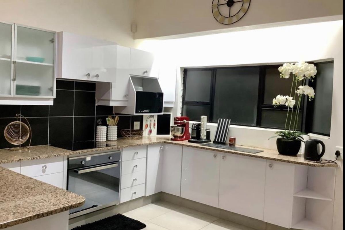 Modern kitchen featuring white gloss cabinetry, granite countertops, a built-in oven, electric hob, and a black tiled backsplash with tiled flooring.