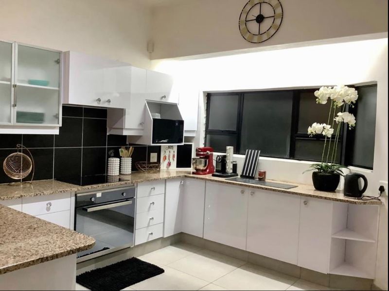 Modern kitchen featuring white gloss cabinetry, granite countertops, a built-in oven, electric hob, and a black tiled backsplash with tiled flooring.