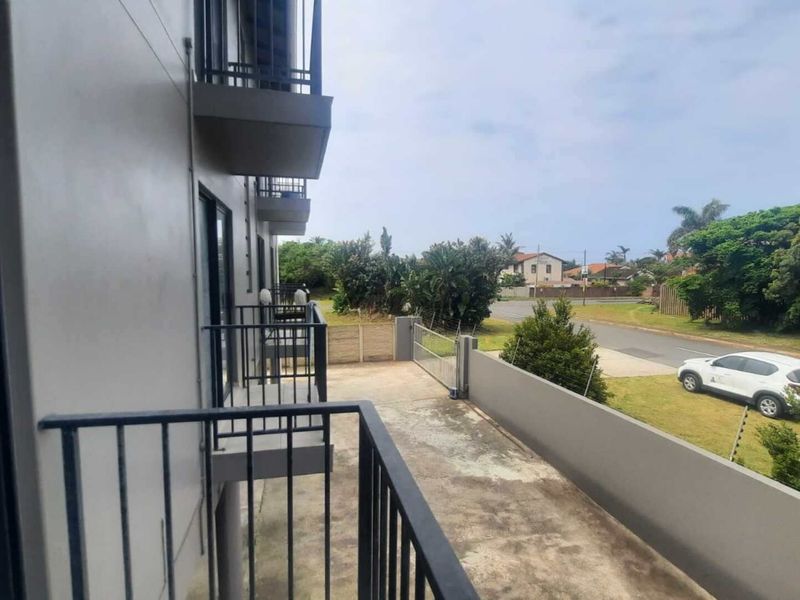 A view from an apartment balcony overlooking the complex grounds, featuring metal railings and concrete flooring with access to the exterior area.
