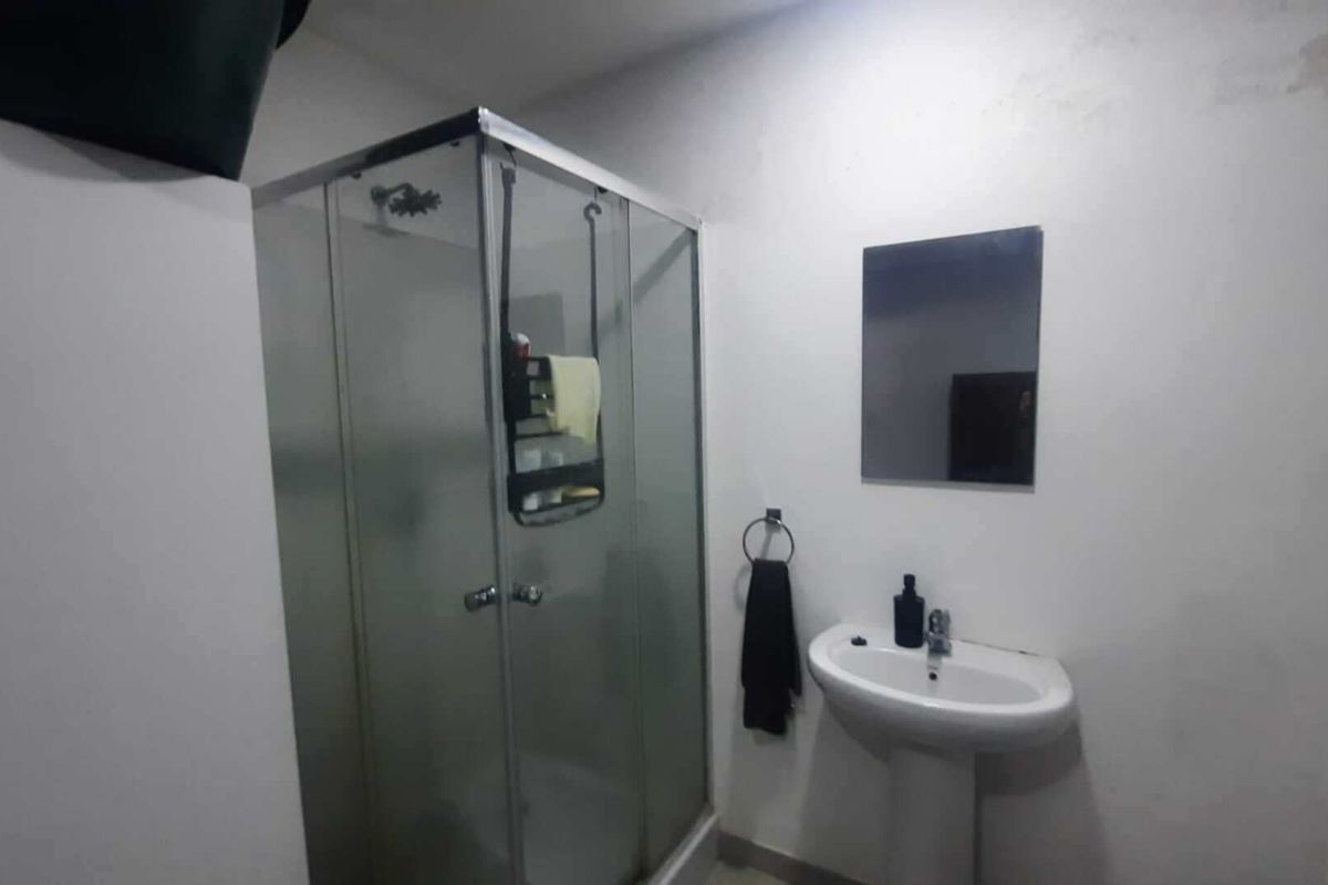 A functional bathroom featuring a glass shower enclosure and a pedestal basin with a wall-mounted mirror.