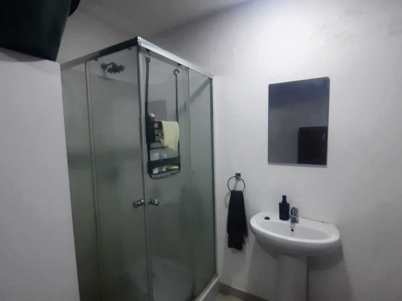 A functional bathroom featuring a glass shower enclosure and a pedestal basin with a wall-mounted mirror.