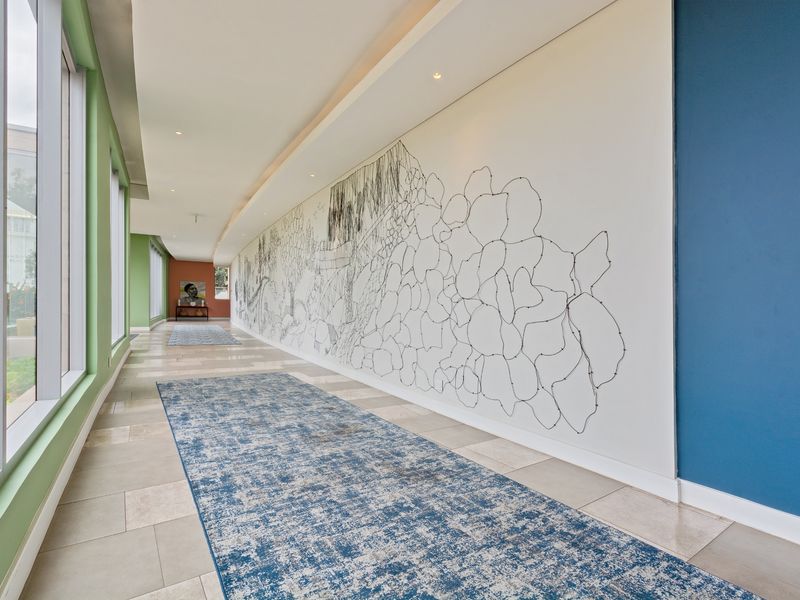 A spacious, well-lit hallway featuring large format floor tiles, floor-to-ceiling windows, and a modern cove ceiling design.