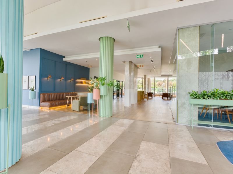 Spacious open-plan communal area featuring modern fluted columns, a mix of tiled and wood flooring, and contemporary glass partitions in a well-maintained building.