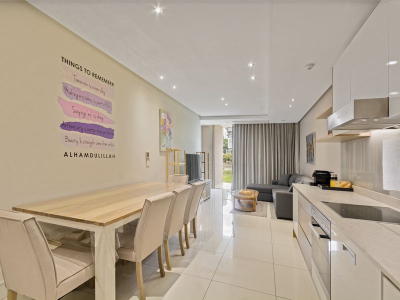 Modern open-plan living area featuring a sleek kitchen with integrated appliances, glossy tiled flooring, and seamless access to a private balcony.