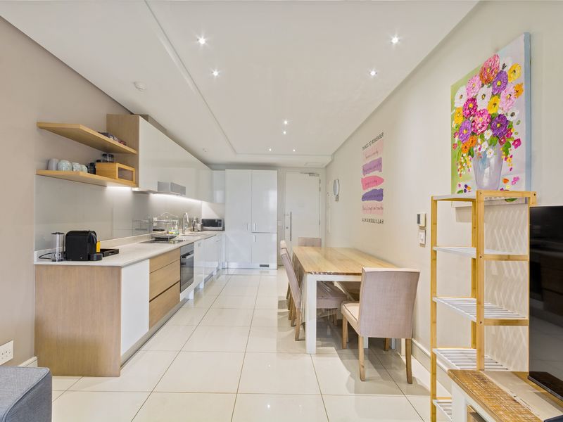 Modern open-plan kitchen and dining area featuring sleek cabinetry, stone countertops, integrated appliances, and bright recessed lighting throughout the space.