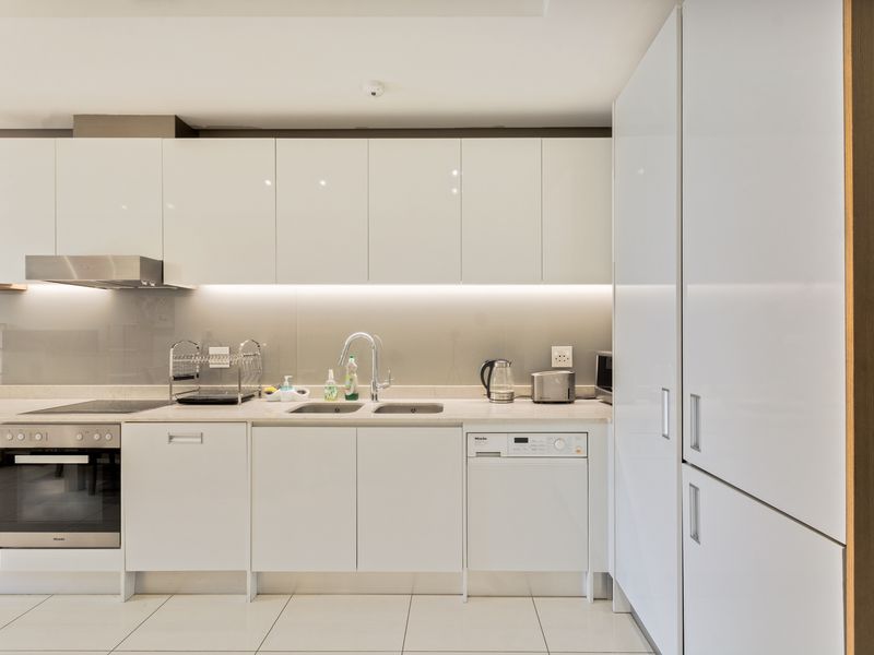 Modern kitchen featuring high-gloss white cabinetry, integrated appliances, stone countertops, and sleek under-cabinet lighting for a clean, contemporary aesthetic.