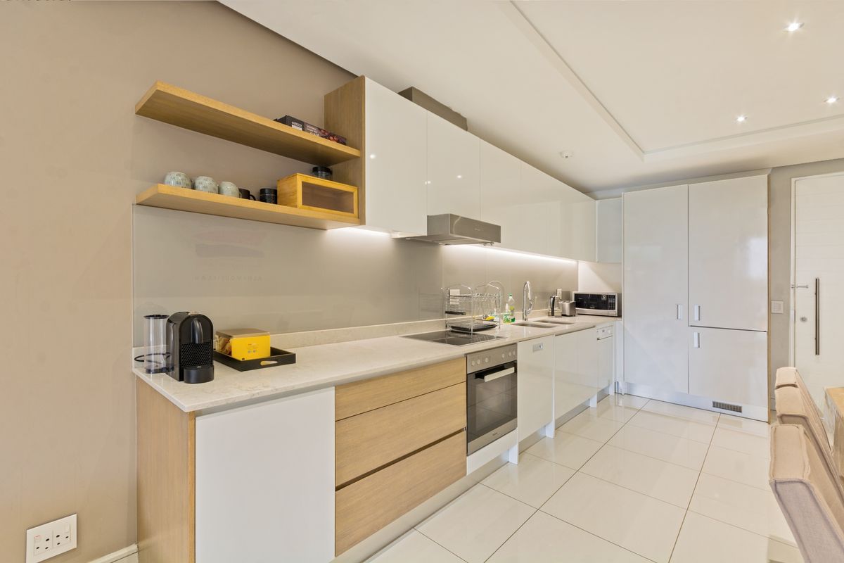 Modern kitchen featuring sleek white and wood-tone cabinetry, stone countertops, integrated appliances, and under-cabinet lighting, finished with polished floor tiles.