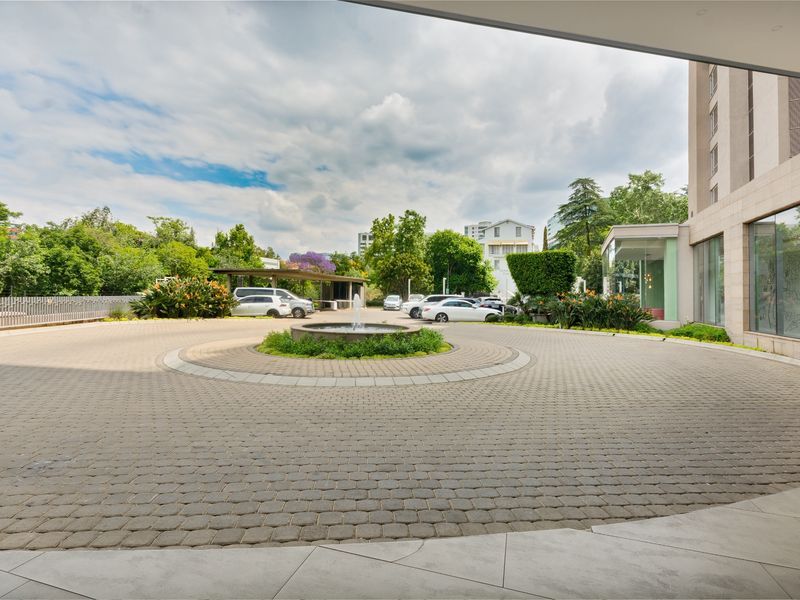 A well-maintained paved circular driveway featuring a central water fountain and landscaped garden, providing an elegant entrance to the apartment building.