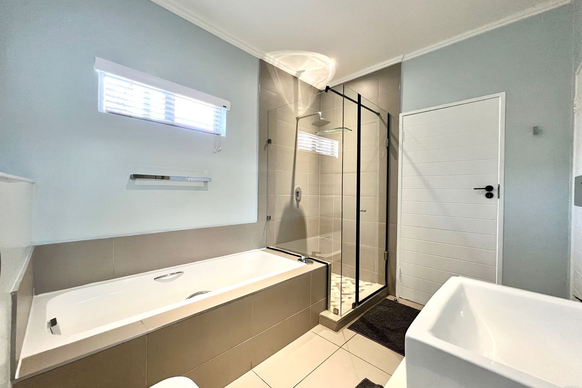 Modern bathroom featuring a built-in bathtub, a separate glass-enclosed shower with a rain shower head, and neutral tiled finishes.
