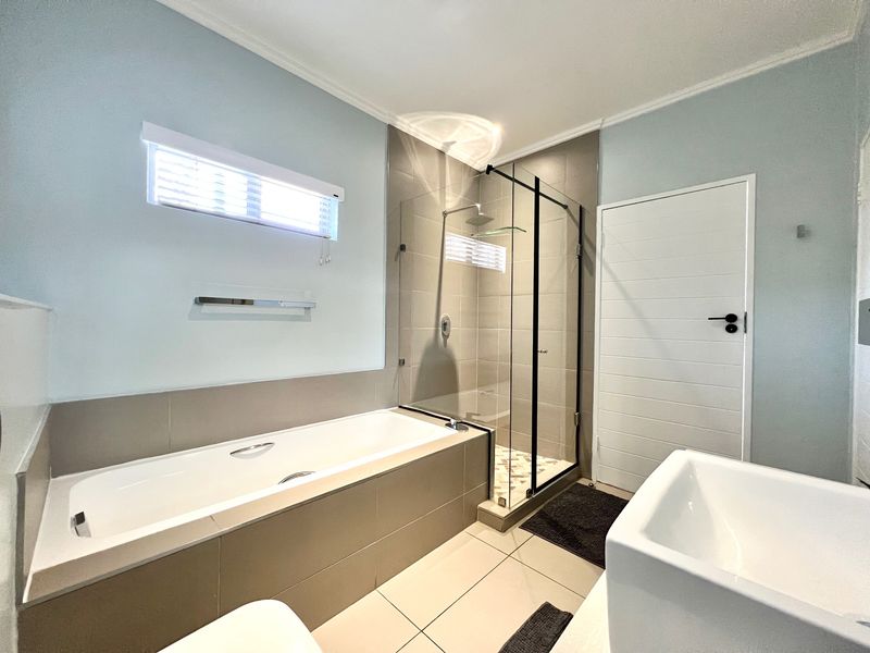 Modern bathroom featuring a built-in bathtub, a separate glass-enclosed shower with a rain shower head, and neutral tiled finishes.