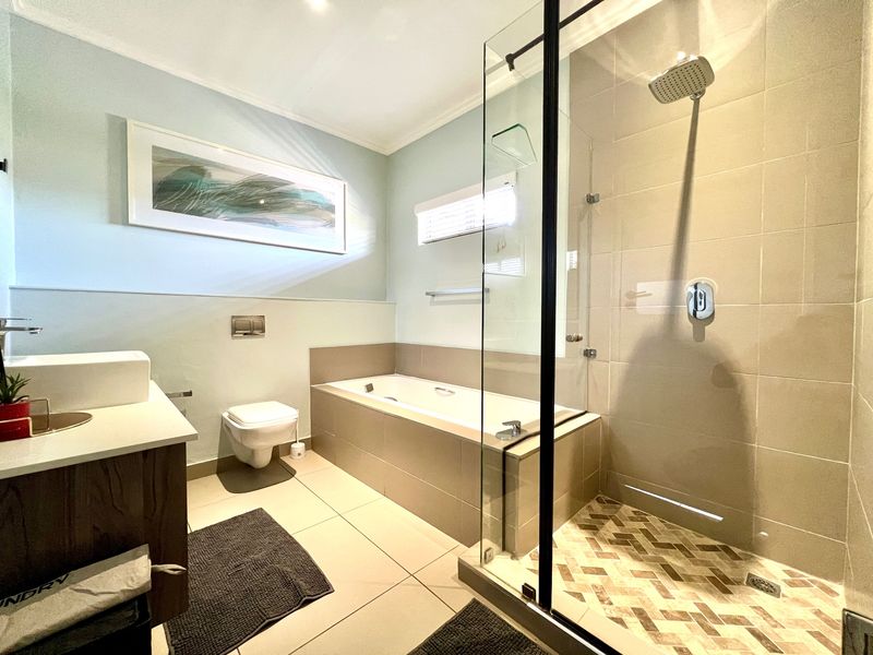 Modern bathroom featuring a glass-enclosed shower, built-in bathtub, wall-mounted toilet, and a sleek vanity with a countertop basin.