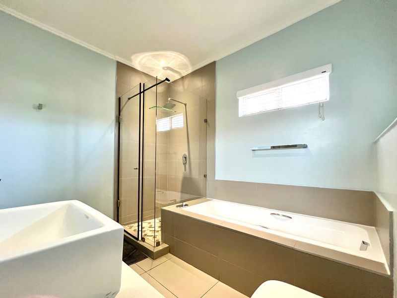 Modern bathroom featuring a glass-enclosed shower, a built-in bathtub, and neutral tiled finishes, offering a clean and functional space.