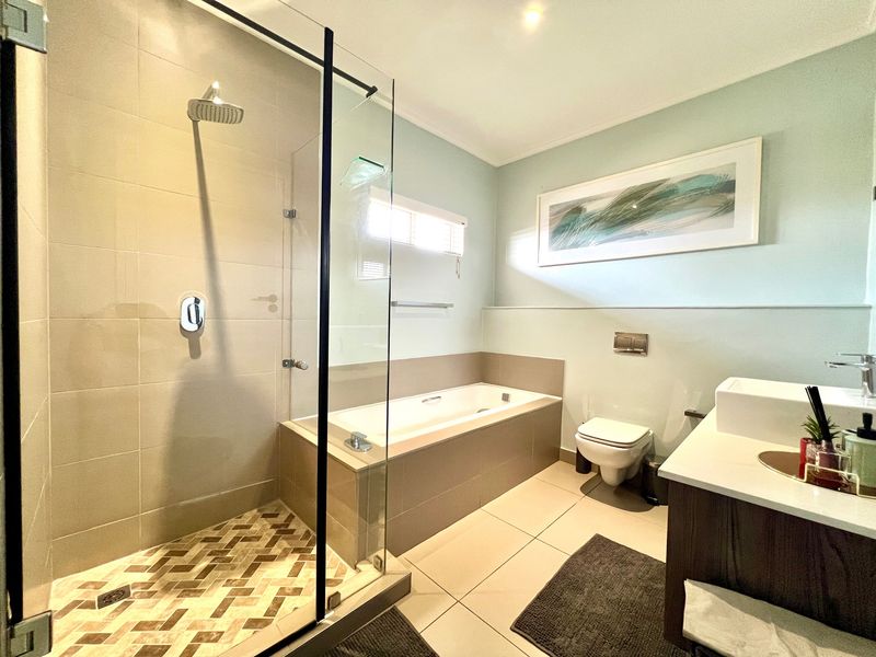 Modern bathroom featuring a walk-in shower with glass screen, built-in bathtub, wall-mounted toilet, and a sleek vanity with countertop basin.