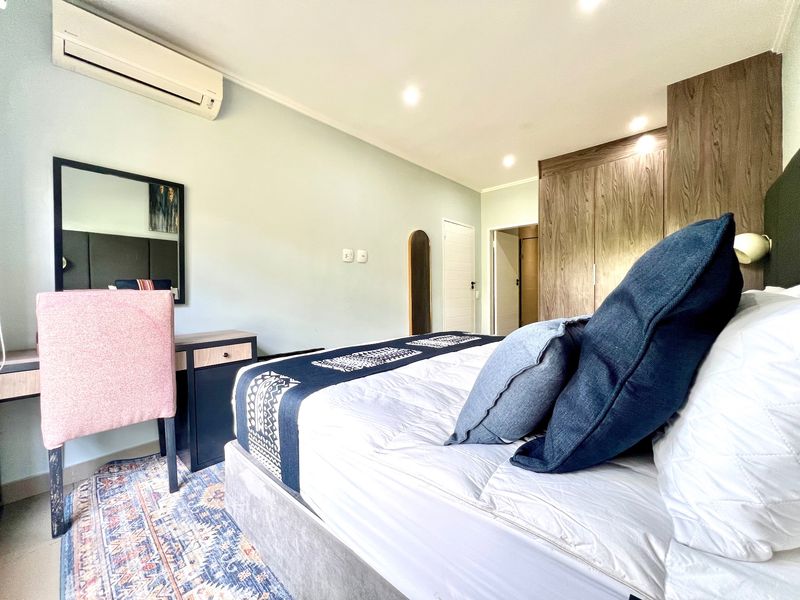 A well-maintained bedroom featuring built-in wooden cupboards, recessed downlighting, and a wall-mounted split-system air conditioning unit.