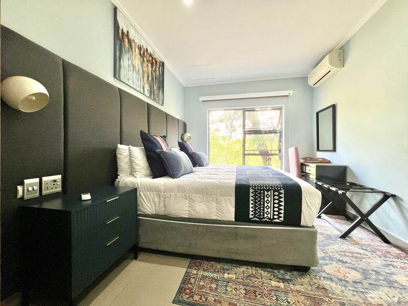 A well-maintained bedroom featuring a large upholstered headboard, wall-mounted air conditioning, and natural light through a sliding window.