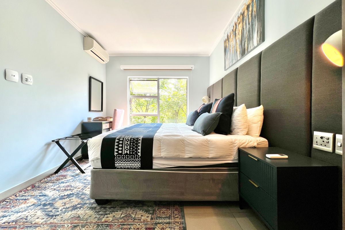 A well-maintained bedroom featuring tiled flooring, an integrated air conditioning unit, and large aluminium-framed windows providing natural light.