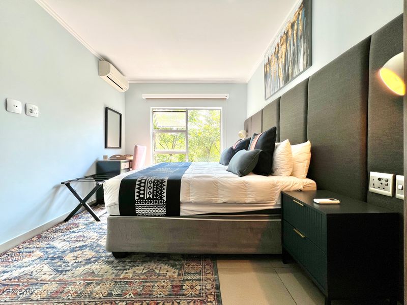 A well-maintained bedroom featuring tiled flooring, an integrated air conditioning unit, and large aluminium-framed windows providing natural light.