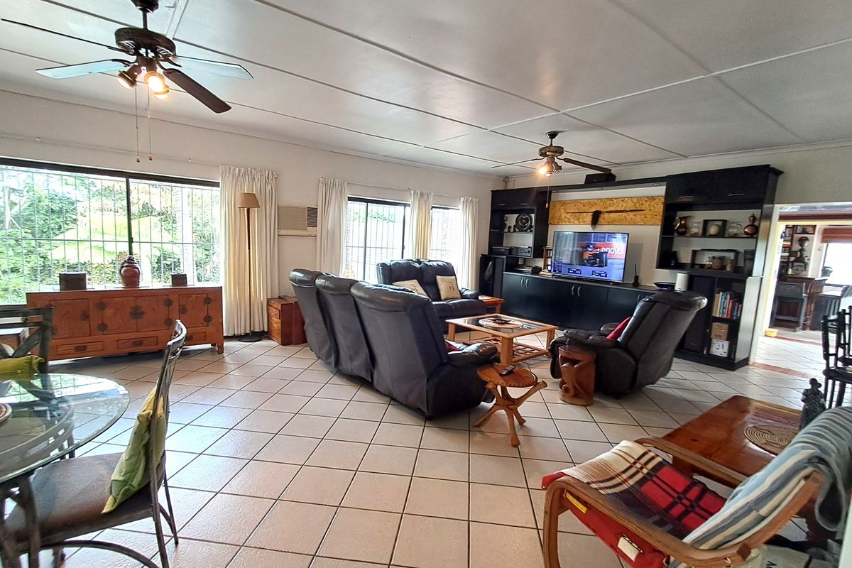 Spacious living room featuring tiled flooring, ceiling fans, and a large built-in entertainment and shelving unit with security bars on the windows.