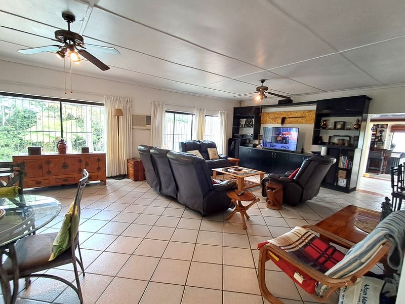 Spacious living room featuring tiled flooring, ceiling fans, and a large built-in entertainment and shelving unit with security bars on the windows.
