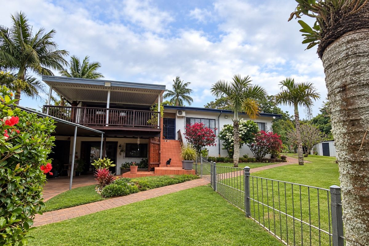 Rear view of the property featuring a raised timber deck, covered patio area, brick staircase, and well-maintained garden with paved pathways.