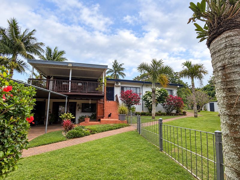 Rear view of the property featuring a raised timber deck, covered patio area, brick staircase, and well-maintained garden with paved pathways.