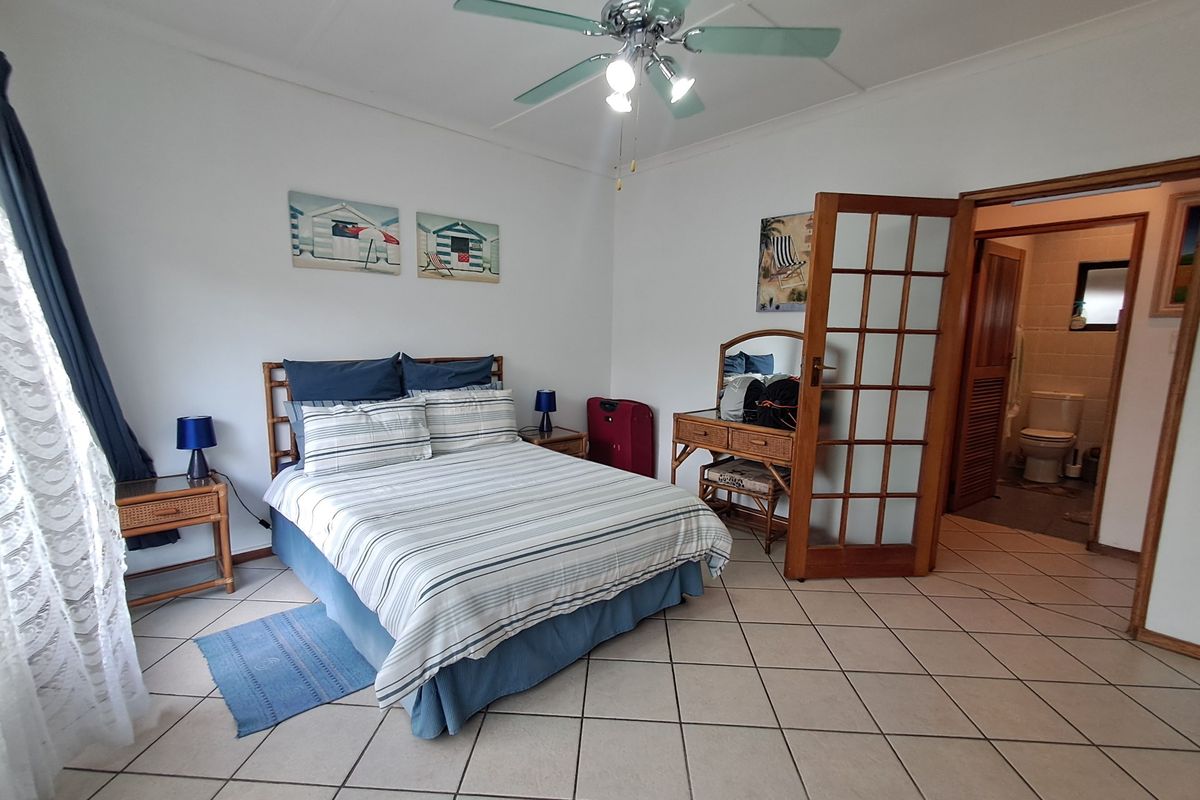 A spacious bedroom featuring tiled flooring, a ceiling fan, and direct access to an en-suite bathroom through a wooden french door.