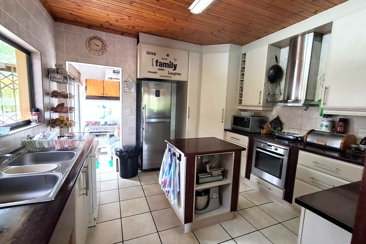 A functional kitchen featuring tiled flooring, timber ceiling, built-in oven, extractor fan, and a central island, offering a practical layout with ample storage.