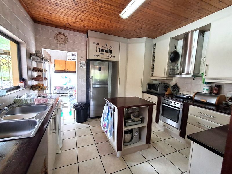 A functional kitchen featuring tiled flooring, timber ceiling, built-in oven, extractor fan, and a central island, offering a practical layout with ample storage.