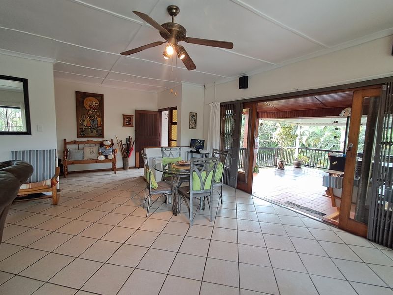Spacious open-plan living and dining area featuring tiled floors, a ceiling fan, and large sliding doors that open onto a covered patio.