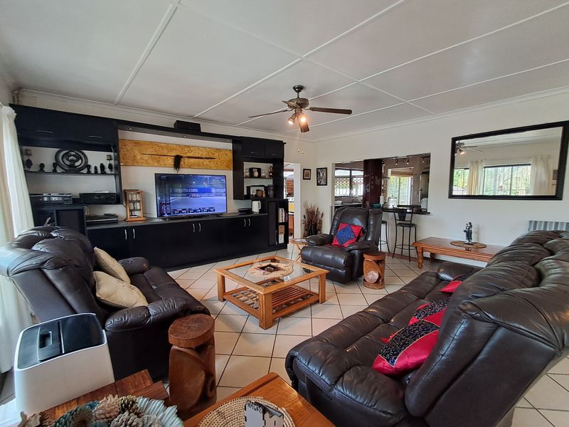Spacious living room featuring built-in cabinetry, tiled flooring, and a ceiling fan, with a convenient pass-through window connecting to the adjacent kitchen area.